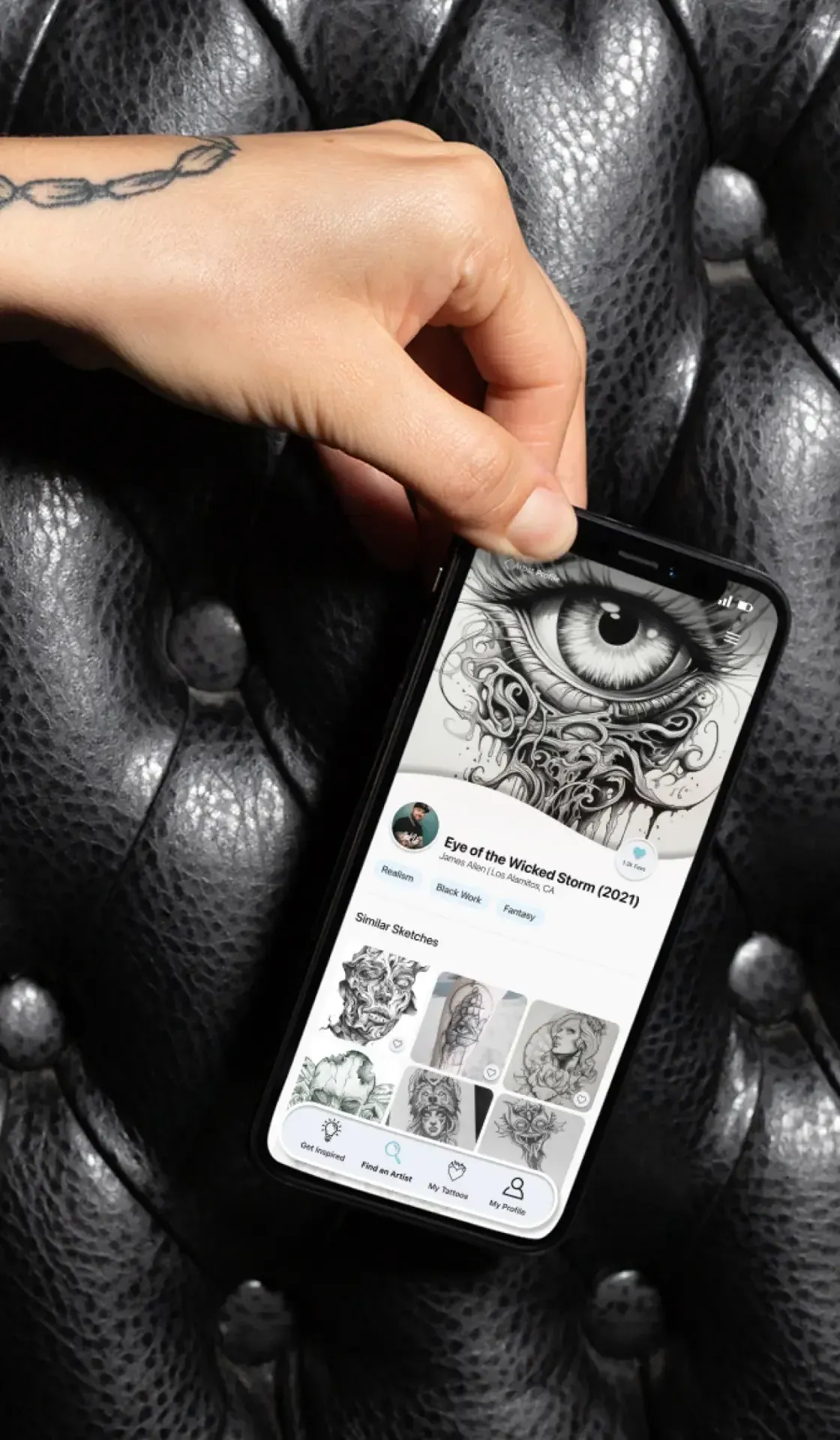 A hand holding a phone running Ink Us against tufted black leather.